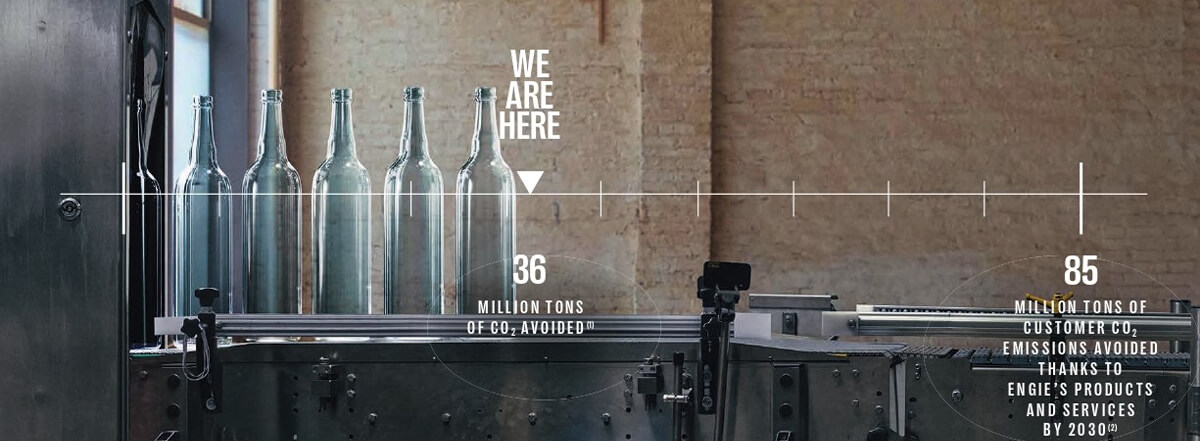 Five glass bottles lined up on a production line in a factory setting.