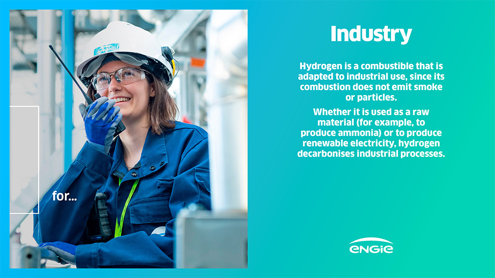A person in a blue work uniform and helmet using a communication device in an industrial setting.