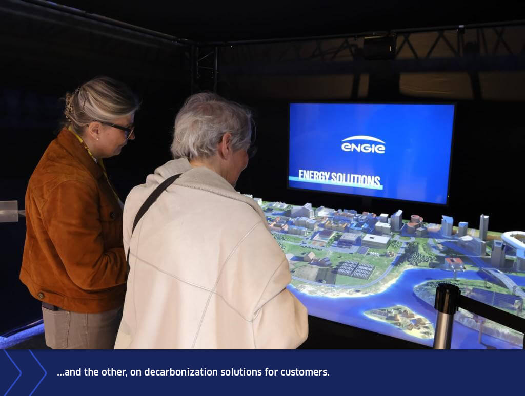 Two visitors observing an interactive scale model presenting ENGIE’s decarbonization solutions for customers during an exhibition at the General Assembly.