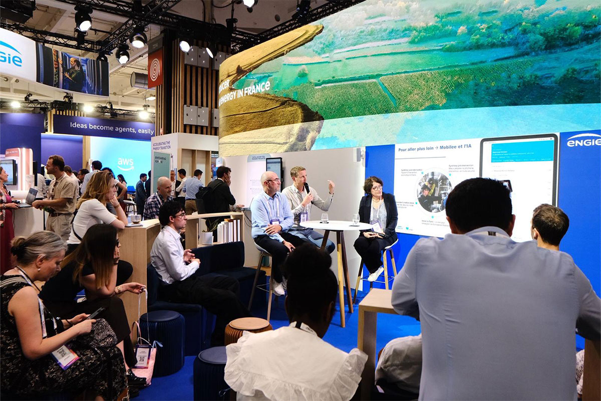 Panel discussion at an energy technology conference booth with attendees seated and digital displays