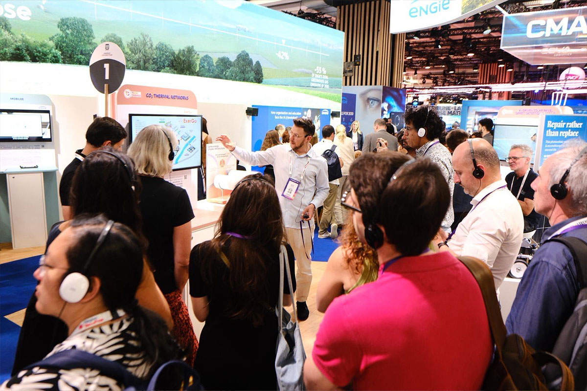 Group of people attending a technology presentation at an exhibition booth with screens and displays