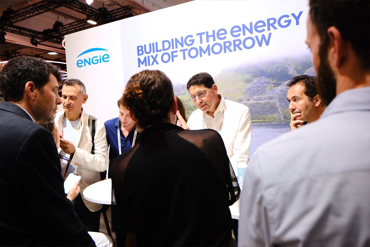 Group of people discussing at an energy company booth with a large display in the background